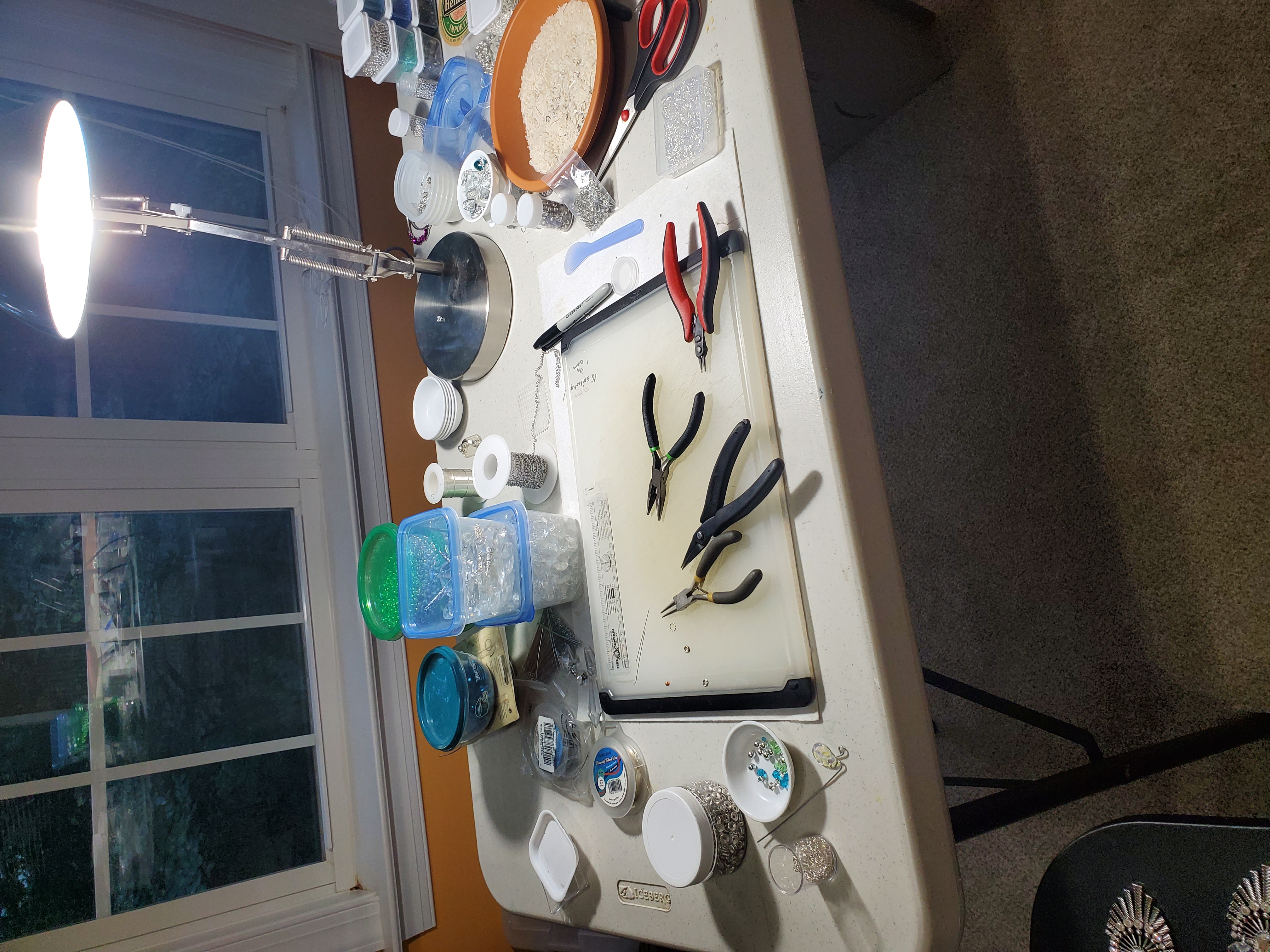 Natural-lit workspace showing jewelry-making tools, pliers, wire, and work surface by the window